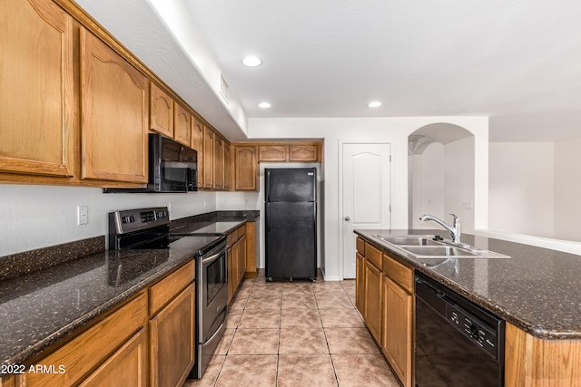 kitchen featuring light tile patterned flooring, black appliances, dark stone counters, a kitchen island with sink, and sink