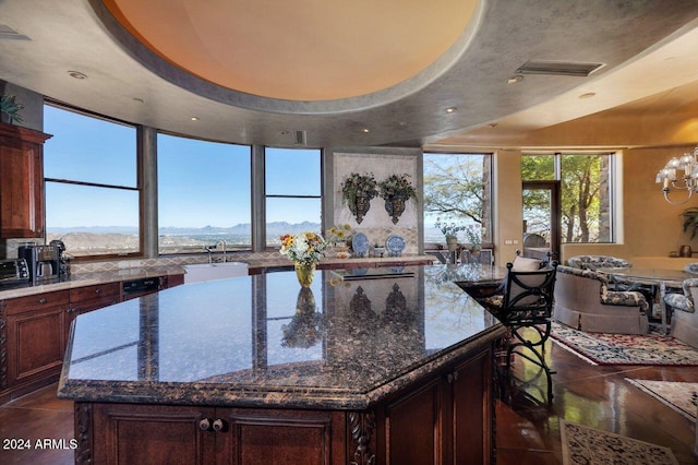 kitchen featuring light stone counters, a raised ceiling, dark tile patterned floors, sink, and a kitchen island