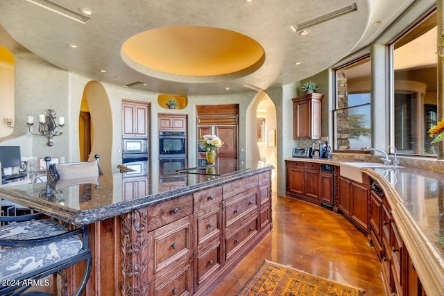 kitchen with a center island, stainless steel microwave, dark stone counters, black electric stovetop, and a raised ceiling