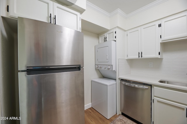 kitchen featuring white cabinetry, stainless steel appliances, backsplash, stacked washer / dryer, and crown molding