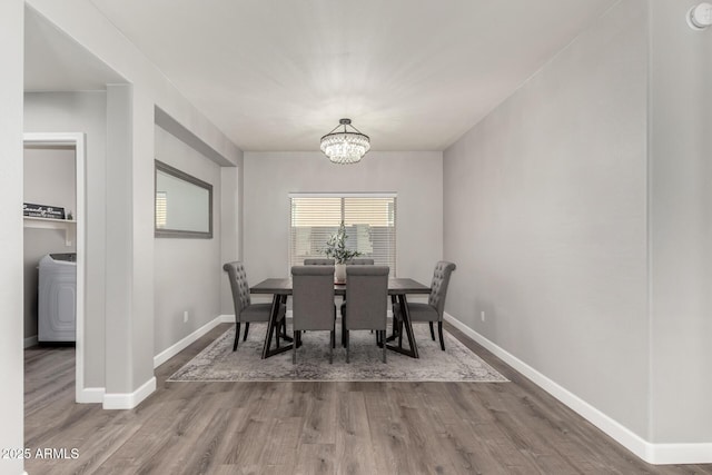 dining area featuring a chandelier, washer / clothes dryer, baseboards, and wood finished floors