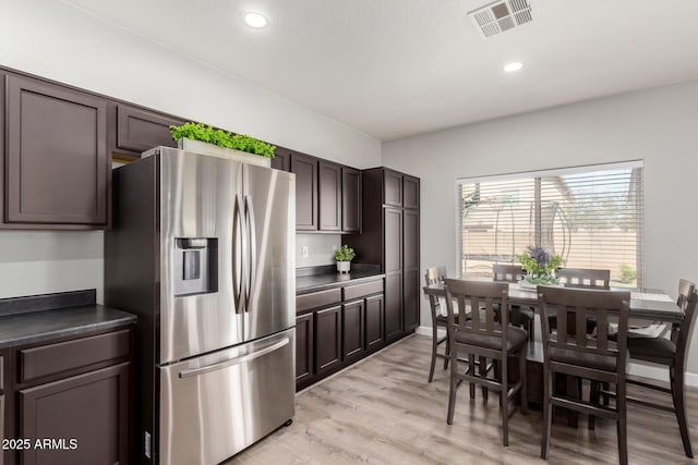 kitchen featuring dark countertops, visible vents, dark brown cabinets, stainless steel fridge with ice dispenser, and light wood-style flooring