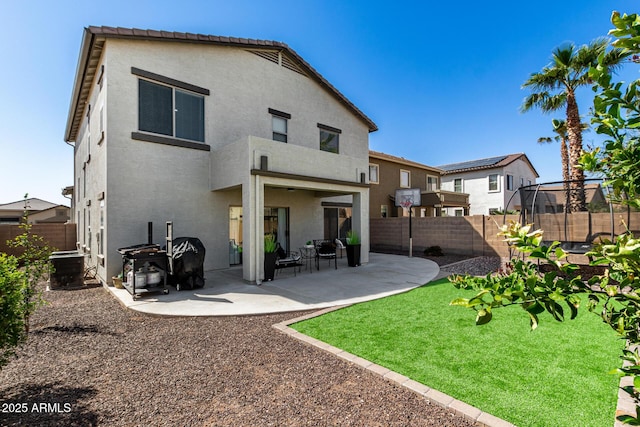 rear view of property featuring a patio, a trampoline, a fenced backyard, and stucco siding