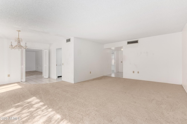 carpeted spare room featuring an inviting chandelier and a textured ceiling