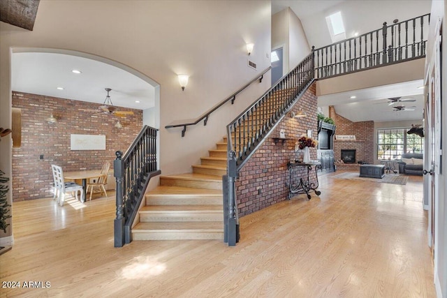 stairway featuring hardwood / wood-style flooring, brick wall, ceiling fan, a large fireplace, and a towering ceiling