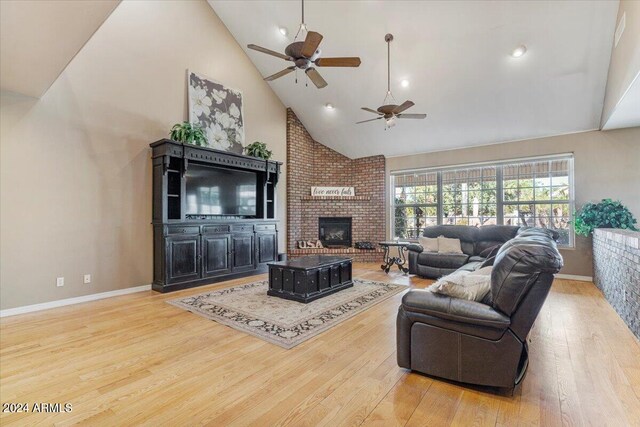 living room with a fireplace, light hardwood / wood-style floors, ceiling fan, and high vaulted ceiling