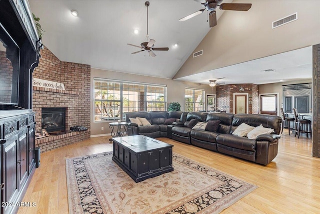 living room featuring a fireplace, ceiling fan, light wood-type flooring, and high vaulted ceiling