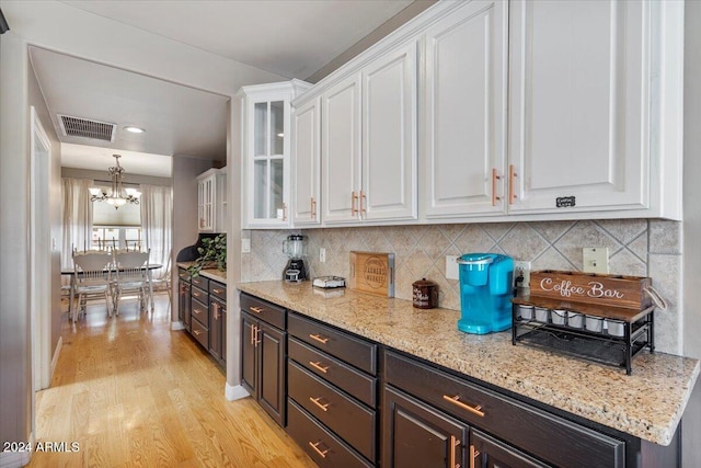 kitchen featuring tasteful backsplash, white cabinetry, light wood-type flooring, light stone countertops, and an inviting chandelier