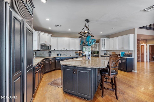 kitchen featuring light hardwood / wood-style floors, white cabinetry, a center island with sink, light stone countertops, and paneled built in fridge