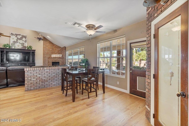 dining space with light wood-type flooring, a fireplace, ceiling fan, and vaulted ceiling