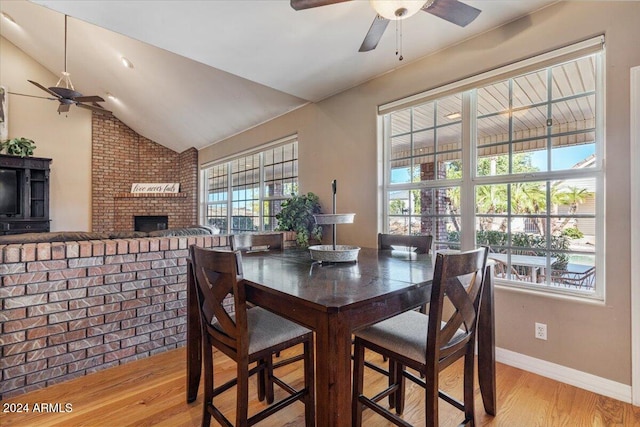 dining room with light wood-type flooring, lofted ceiling, brick wall, and ceiling fan