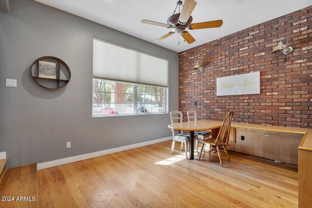 dining area with light hardwood / wood-style floors, ceiling fan, and brick wall