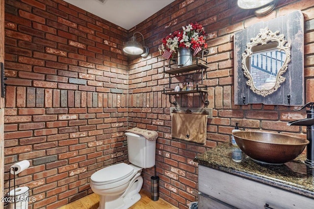 bathroom with toilet, vanity, hardwood / wood-style flooring, and brick wall