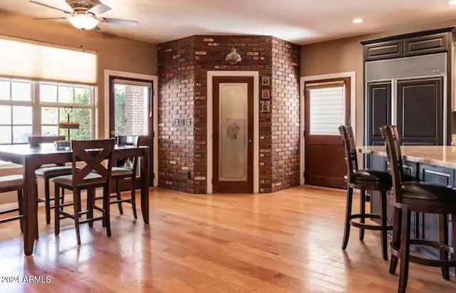 dining area with brick wall, a wealth of natural light, ceiling fan, and light hardwood / wood-style flooring