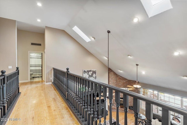 hallway with high vaulted ceiling, light hardwood / wood-style floors, and a skylight