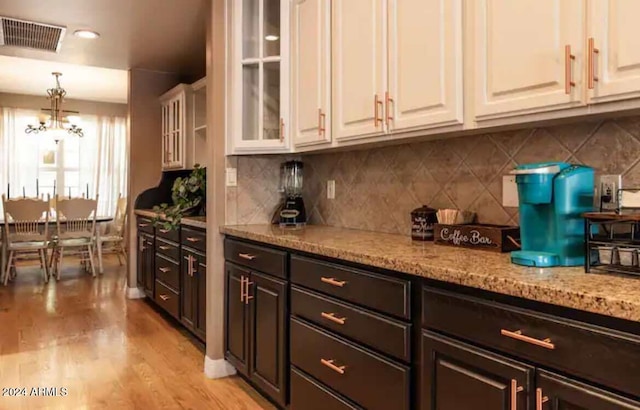 kitchen with white cabinetry, dark brown cabinets, light stone countertops, a chandelier, and light hardwood / wood-style flooring