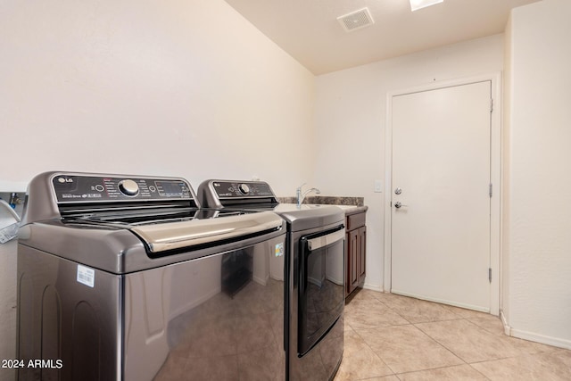 clothes washing area with cabinets, light tile patterned floors, and washer and clothes dryer