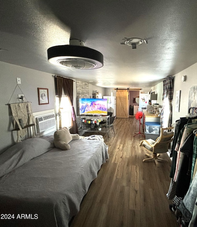 bedroom with a textured ceiling, cooling unit, wood-type flooring, and a barn door