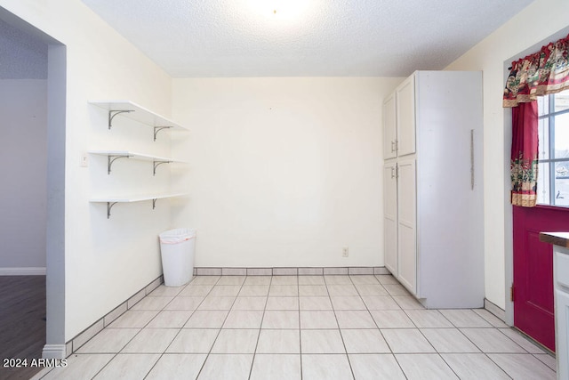 interior space with light tile patterned flooring, a textured ceiling, and white cabinets