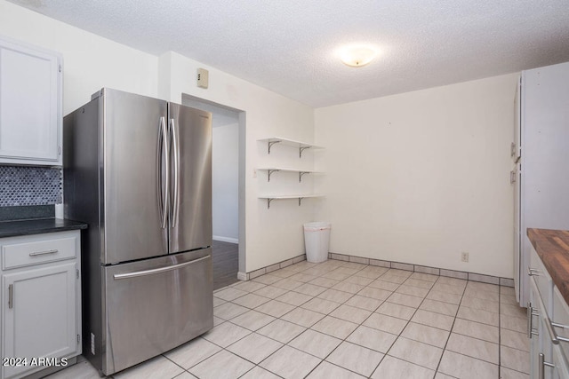 kitchen with light tile patterned floors, decorative backsplash, stainless steel refrigerator, a textured ceiling, and white cabinetry