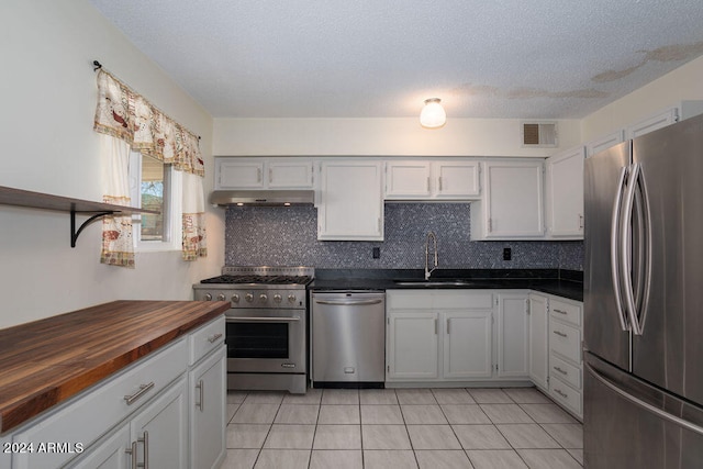 kitchen featuring decorative backsplash, wood counters, light tile patterned floors, sink, and stainless steel appliances