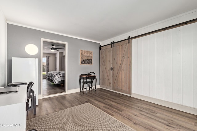 interior space featuring crown molding, baseboards, a barn door, and wood finished floors