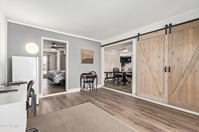 interior space with ornamental molding, baseboards, a barn door, a ceiling fan, and wood finished floors