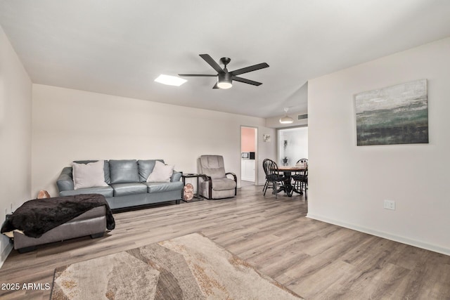 living room with baseboards, visible vents, wood finished floors, and a ceiling fan
