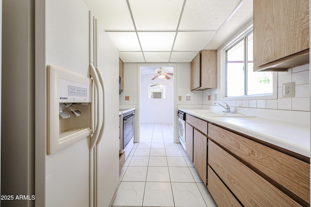 kitchen featuring ceiling fan, a drop ceiling, white refrigerator with ice dispenser, light countertops, and a sink