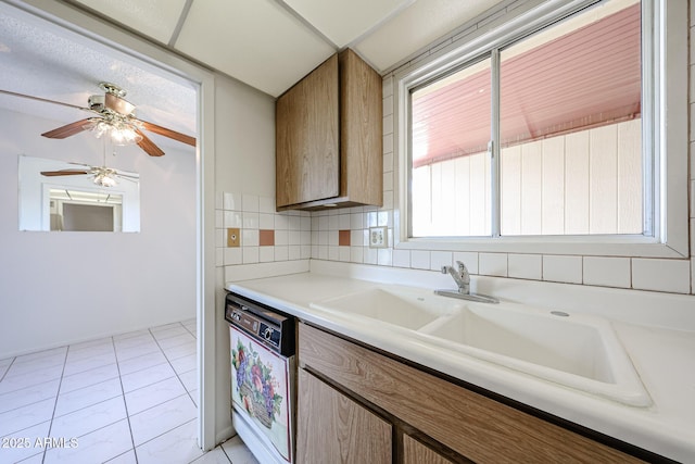 kitchen featuring ceiling fan, dishwasher, a sink, light countertops, and light tile patterned flooring