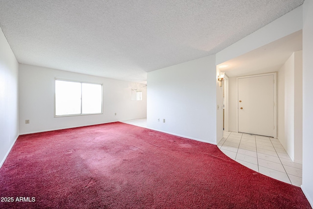 empty room with baseboards, a textured ceiling, light colored carpet, and light tile patterned floors