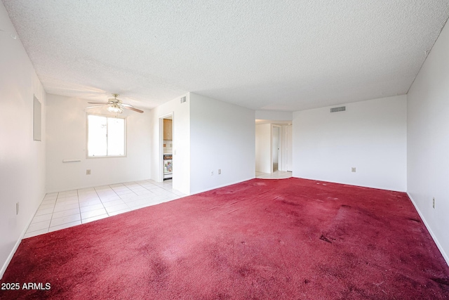 carpeted empty room featuring a ceiling fan, a textured ceiling, visible vents, and tile patterned floors
