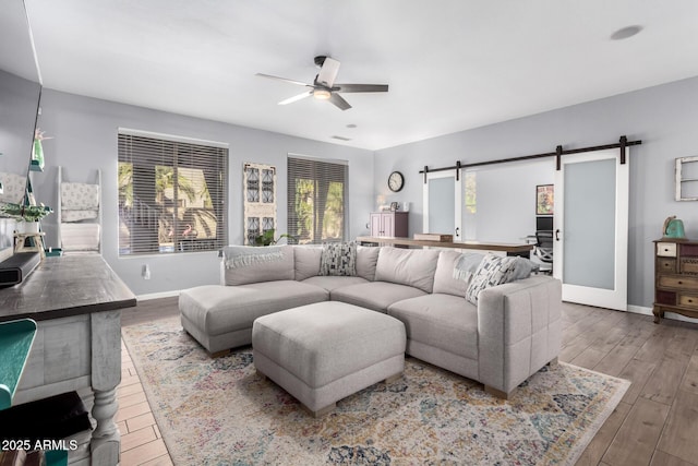 living room featuring ceiling fan, light hardwood / wood-style flooring, and a barn door