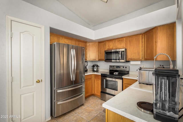 kitchen with appliances with stainless steel finishes, vaulted ceiling, and light tile patterned flooring