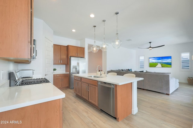 kitchen with light hardwood / wood-style floors, hanging light fixtures, sink, an island with sink, and appliances with stainless steel finishes