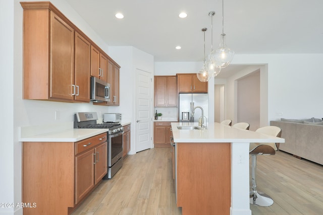 kitchen with stainless steel appliances, sink, a breakfast bar, hanging light fixtures, and light wood-type flooring