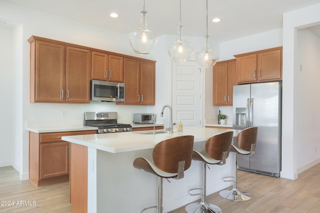 kitchen featuring light hardwood / wood-style floors, sink, appliances with stainless steel finishes, hanging light fixtures, and a kitchen island with sink