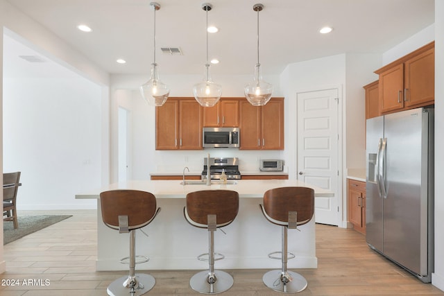 kitchen featuring stainless steel appliances, a kitchen island with sink, pendant lighting, and light hardwood / wood-style floors