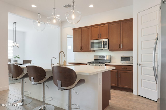 kitchen featuring light hardwood / wood-style floors, a center island with sink, sink, appliances with stainless steel finishes, and decorative light fixtures