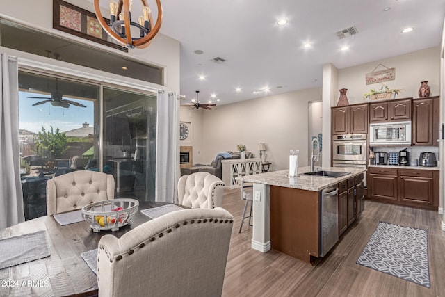 kitchen with a center island with sink, sink, dark hardwood / wood-style floors, light stone countertops, and stainless steel appliances