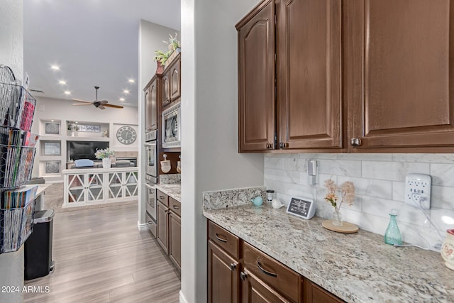 kitchen featuring stainless steel microwave, backsplash, ceiling fan, light stone countertops, and light wood-type flooring