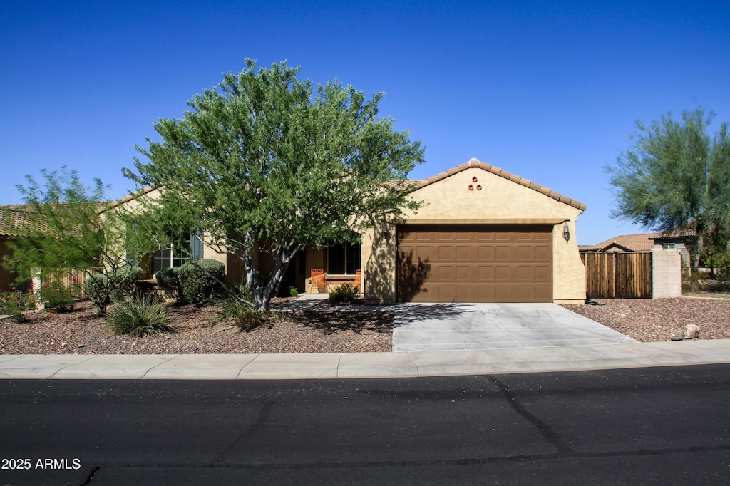 view of front facade with an attached garage, fence, a tile roof, driveway, and stucco siding