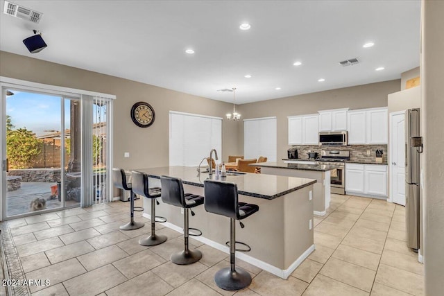 kitchen featuring dark stone counters, sink, decorative backsplash, an island with sink, and appliances with stainless steel finishes