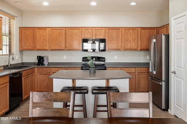 17802 N 114th Ln, Surprise, AZ 85378 - kitchen featuring black appliances, a sink, a kitchen breakfast bar, light wood finished floors, and a center island