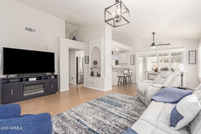 living room with ceiling fan with notable chandelier, lofted ceiling, and light wood-type flooring