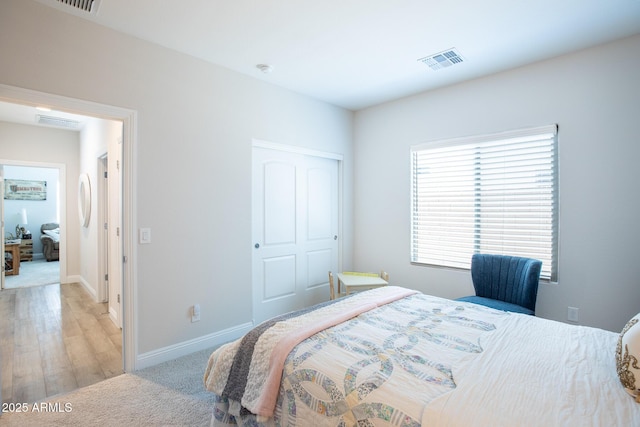 bedroom featuring visible vents, baseboards, light wood finished floors, and light colored carpet