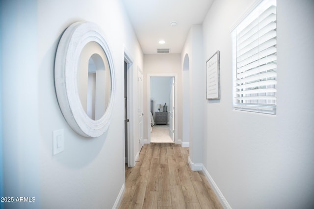corridor featuring baseboards, arched walkways, light wood finished floors, and visible vents