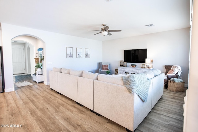 living area featuring visible vents, arched walkways, light wood finished floors, and ceiling fan