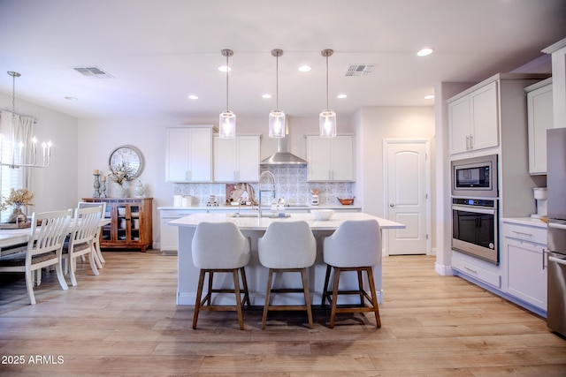 kitchen with light countertops, appliances with stainless steel finishes, wall chimney exhaust hood, and visible vents