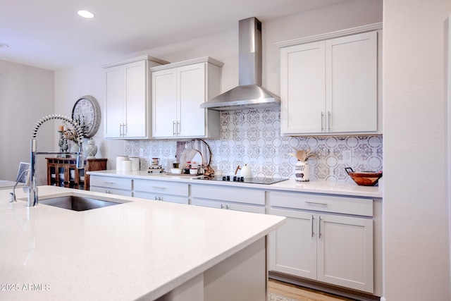 kitchen with black electric stovetop, a sink, light countertops, wall chimney exhaust hood, and backsplash